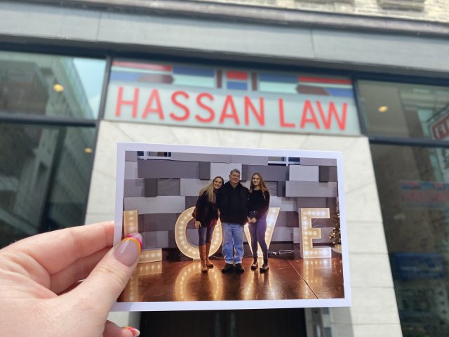 A printed photo of Hamoody Hassan and his family is held up in front of the Hassan Law building.