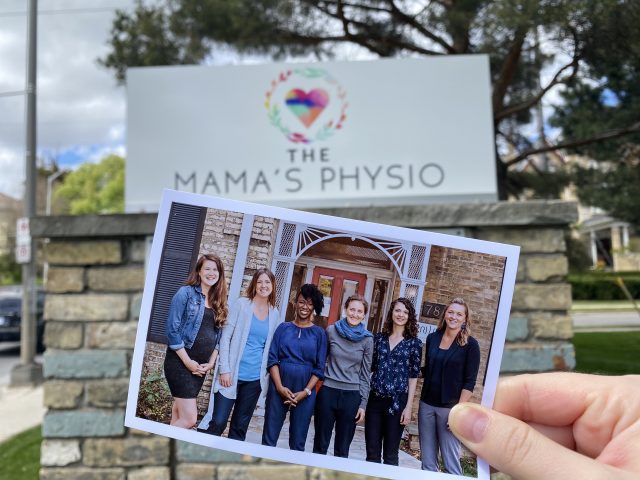 A printed photo of the Mama's Physio team is held up in front of the business's sign