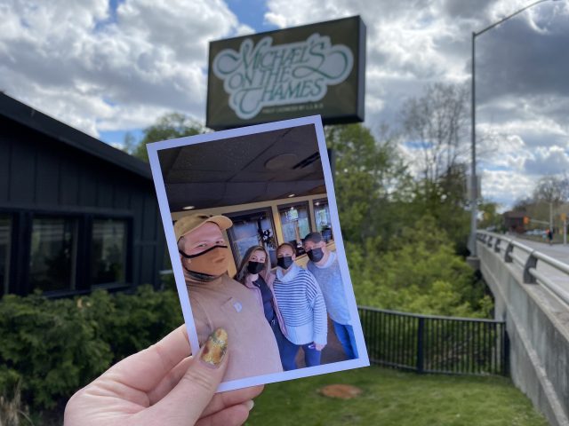 A printed photo of Michael's On The Thames staff and family is held up in front of the restaurant.