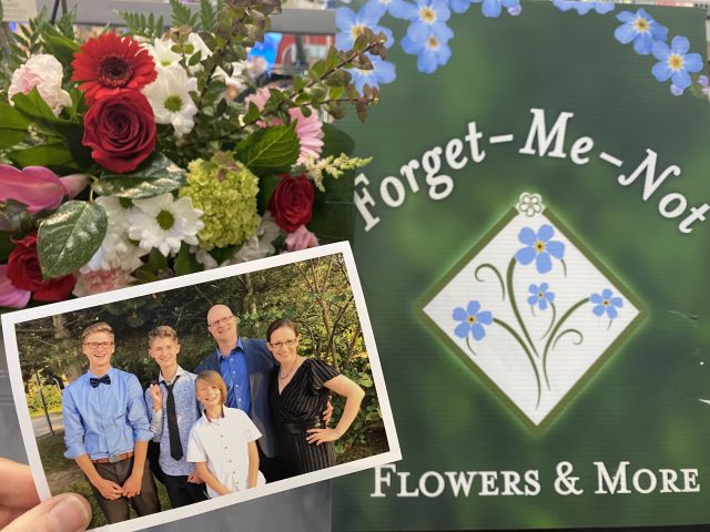 A printed photo of Natasha Sumner and her family held up in front of Forget-Me-Not Flowers, her family business.