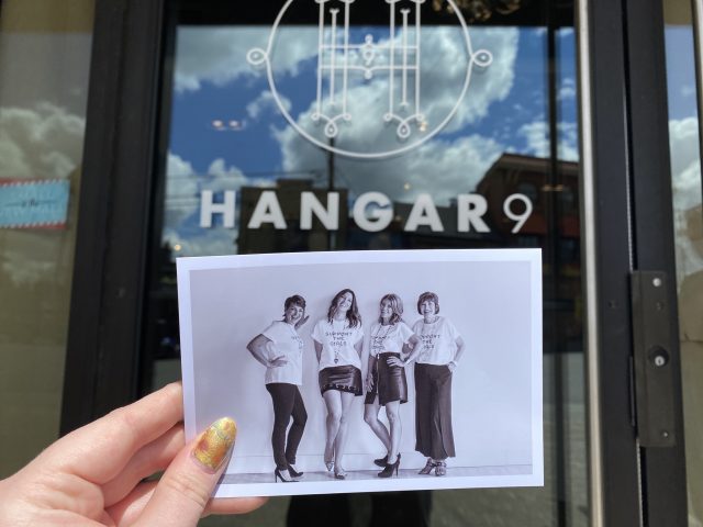 A printed photo of the staff is helf up in front of the Hangar9 storefront.