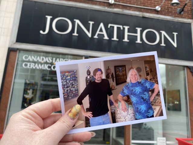 A printed photo of Jonathon Bancroft-Snell and Brian is held up in front of their storefront Jonathon's