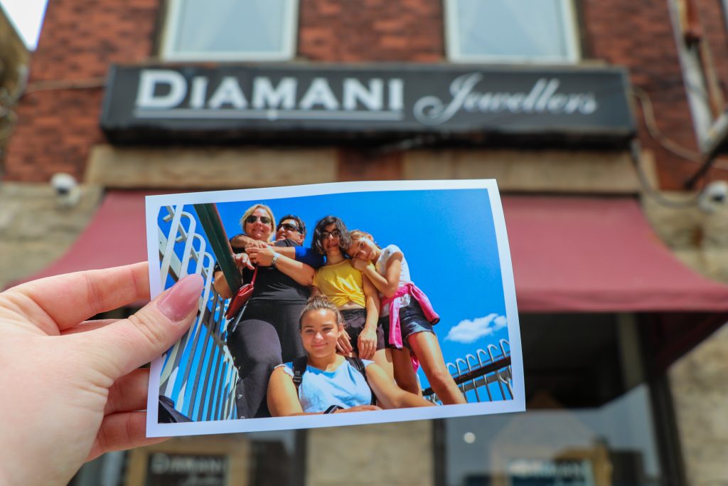 A printed photo of Mario Chirico and his family is held up in front of his storefront on 432 Clarence Street, Diamani Jewellers