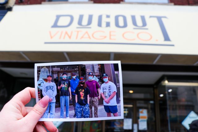 a printed picture of the DugOut team is held up in front of the store and marquee. 