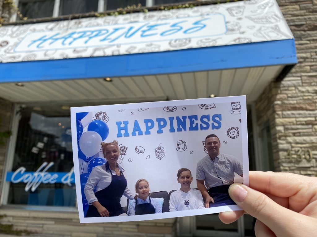 A printed photo of the owner's family is held up in front of the Happiness Cafe