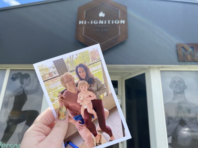 A printed photo of April and her family is held up in front of the Hi Ignition Fit Lab sign.